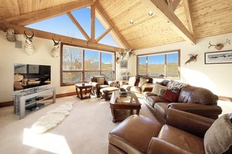 A large living room with a vaulted ceiling, leather sofas, and a large window with a view of the mountains.