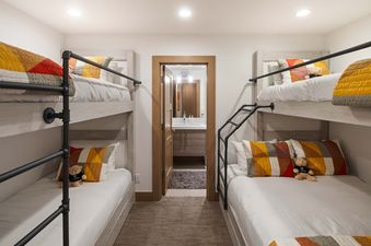 A cozy bunk room at Silver Lode Escape with four beds, each adorned with white bedding and colorful patterned quilts, and a peek into a modern bathroom beyond.