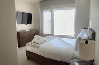 Modern and minimalist bedroom in the Lift 4 Bedroom Suite featuring a large bed, dresser, and wall-mounted TV.
