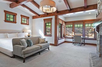A spacious bedroom at Solstice at Empire Pass features a large bed, a comfortable sofa, a cozy fireplace, and multiple windows offering a view of the outdoors.