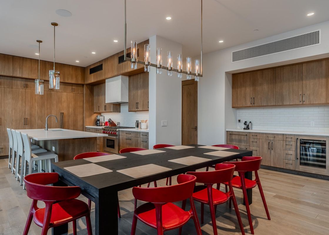 The dining area of Moonlight Basin 7 Speedwell Drive, featuring a large, black dining table with red chairs and a modern chandelier.