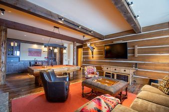 The games room at 492 Golf Course Circle features a billiards table, a mounted deer head, a flatscreen TV, and comfortable seating, all under a rustic beamed ceiling.