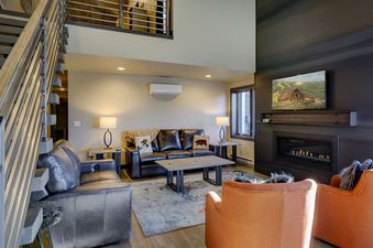 A modern living room with a black leather sofa, orange chairs, and a fireplace.