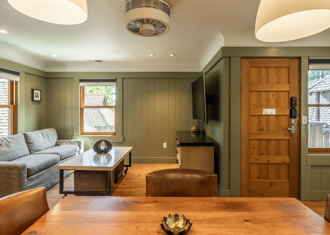 A cozy living room in Cedar Crest Mallard Cottage 5 features a grey sofa, a marble coffee table, and green paneled walls, with natural light streaming through multiple windows.