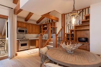 An inviting kitchen and dining area in Villa Valhalla 9, featuring rustic wooden cabinetry, modern stainless steel appliances, and a round wooden dining table with unique antler decor, all illuminated by a stylish pendant light.