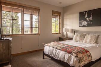 A serene bedroom at Moonlight Mountain 8 Happy Trails with a comfortable bed, large windows showcasing an outdoor view, and rustic decor.