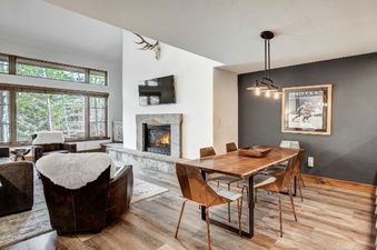 The living area within Arrowhead Village Condominium Premium 2 Bedroom and Loft features a cozy fireplace, comfortable seating, and a dining area, all with large windows offering a view of the natural surroundings.