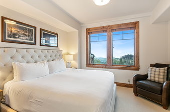 King-sized bed in a bedroom with a mountain view and a chair with plaid throw pillows.