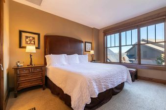 A bedroom with a king sized bed, a dresser next to it, and a large window overlooking the mountains.