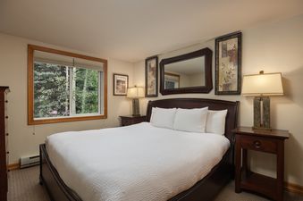 A master bedroom at Terracehouse 63 features a large bed with dark wood furniture, white bedding, and two bedside lamps, complemented by a window with a green outdoor view and framed artwork.