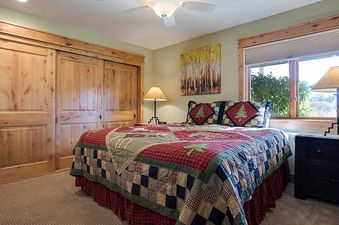 A secondary bedroom with a bed featuring a red and blue patterned quilt, decorative pillows, wooden sliding closet doors, and a window with an outdoor view.