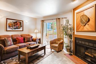An inviting living room in Powder Pointe 201A, featuring a brown sofa, a wooden coffee table, an armchair, and a fireplace, with a sliding door leading to a balcony.