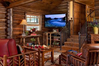 Cozy living room in a rustic log cabin with leather armchairs and a wall-mounted TV.