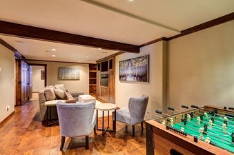 A game room with a foosball table, two armchairs, a couch, and a built-in entertainment center with a TV.