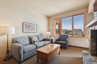 The inviting living area in Morning Eagle 207 features a gray sofa, a wooden coffee table, an armchair by a large window, and ambient lighting from floor and table lamps.