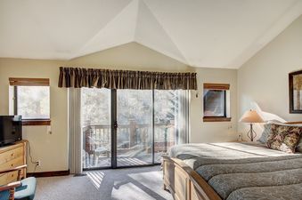 A bedroom with a king-sized bed, a large window overlooking a wooded area, and a TV in the corner.