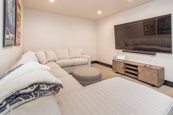 A cozy media room featuring a large sectional sofa, a flat-screen TV mounted above a wooden media console, and movie posters on the wall.