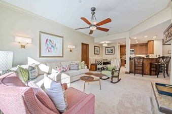 A spacious and brightly lit open-concept living room, dining area, and kitchen of The Charter D280, featuring comfortable seating, modern decor, and rich wooden finishes.