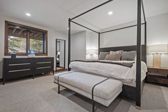 A large, comfy bed dominates this bedroom, which also has a dresser and a tall mirror. The room features a window providing a view of the surrounding trees.