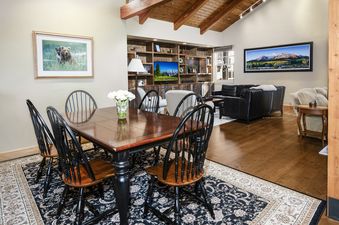 A dining table with black chairs in the foreground of a spacious living area with vaulted wooden ceilings inside Buffalo Park 3.