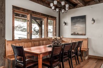 A rustic yet elegant dining area at Latigo Lodge, featuring a long wooden table, leather chairs, and a unique candle centerpiece, with large windows overlooking a snow-covered landscape.