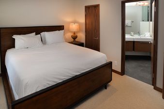 A comfortable bedroom with a queen-sized bed, and an open doorway leading to a well-lit bathroom.