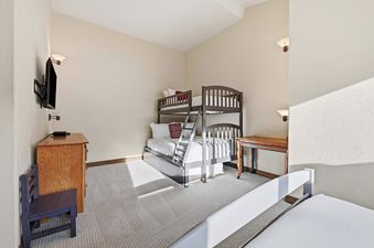 A bunk bedroom at Highlands Slopeside 502 featuring a wooden bunk bed, a dresser with a TV mounted above it, and a small colorful desk.
