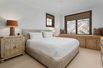 A serene bedroom in Silver Strike Lodge 705 features a king-sized bed with white linens, a distressed nightstand, and a window seat offering stunning mountain views.
