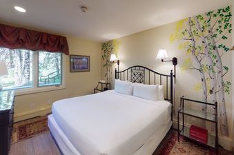 The bedroom at Manor Vail 081 features a king-size bed, a side table with a lamp, and a window with a view of the trees. The room is decorated with a nature-themed mural on the wall.