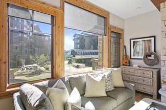 The living room of Silver Strike Lodge 302 with a gray sofa, throw pillows, and a large window offering a view of the Silver Strike Express ski lift and buildings.