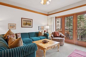 The living area at The Charter C3305 features a blue striped sofa, a wooden coffee table, and an armchair by a balcony with a snowy outdoor view.