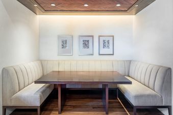 A cozy dining nook at 24 Little Cloud Trail features U-shaped banquette seating, a dark wood table, abstract art, and a tray ceiling with recessed lighting and a herringbone wood inlay.