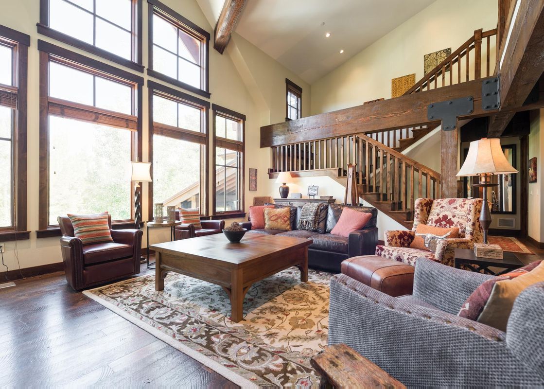 The grand living area of Silver Star 04 features high ceilings, a comfortable seating arrangement with leather and patterned chairs, a wooden coffee table, and an impressive staircase leading to an upper level, all bathed in natural light from large windo