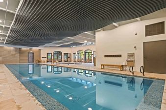 The indoor pool at The Charter C1305 features refreshing blue water, a bright and airy atmosphere with arched windows offering outdoor views, and a unique wavy ceiling design.