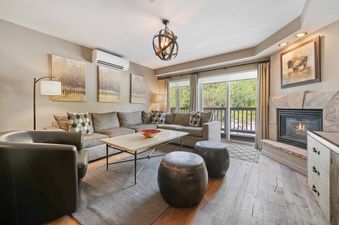 A spacious and inviting living room at St James Place 235 with comfortable seating, a fireplace, and large windows offering a lush exterior view.