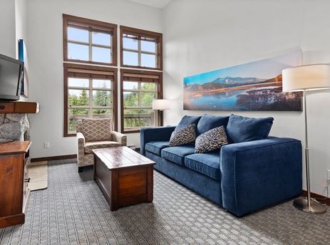The living area of Blackcomb Springs Studio is equipped with a blue sofa, a wooden coffee table, a television atop a wooden cabinet, and a fireplace, offering a cozy and functional space for relaxation.