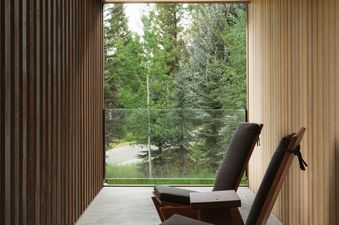 A serene outdoor balcony at Caju featuring dark wooden lounge chairs with charcoal cushions, offering a view of a lush forest.