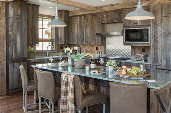 A rustic yet modern kitchen with wooden cabinetry, a large island with a light countertop, and bar stools, ready for entertaining.