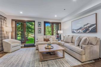 A cozy living room at Woodrun Place 40 featuring an L-shaped sofa, an armchair, a coffee table, and large sliding glass doors opening to a lush outdoor view.