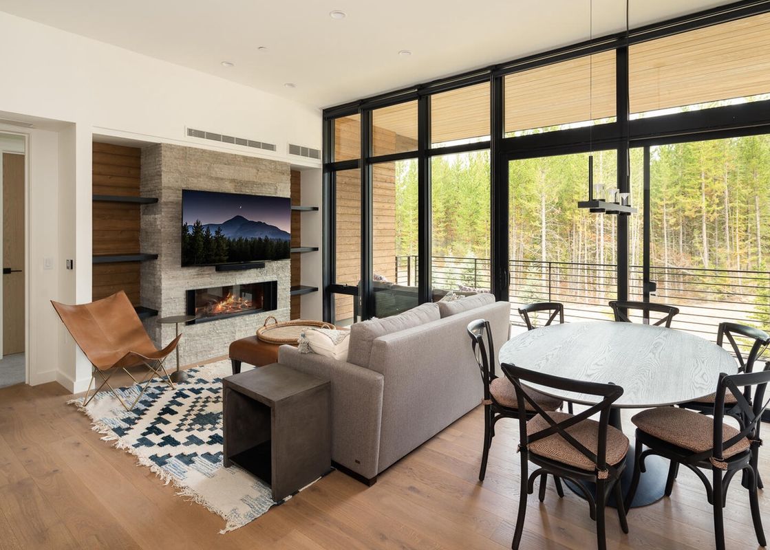 Living room of Moonlight Basin 221 Lakelodge with a modern fireplace, sectional couch, and windows with a view of trees.