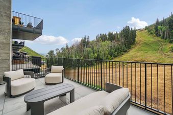 An outdoor patio at Founders Place 2401 with modern furniture and a stunning view of a forested mountain and ski slope.