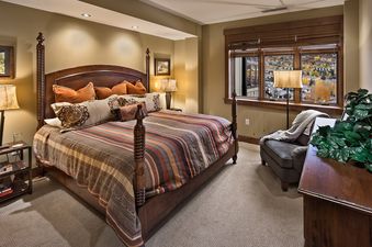 A cozy bedroom with a large wooden four-poster bed, striped bedding, and two nightstands with lamps.