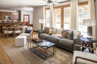 A spacious, open-concept living area in Essentia Townhome 167A features a lounge with a gray sofa, a dining area, and a kitchen with wooden accents.