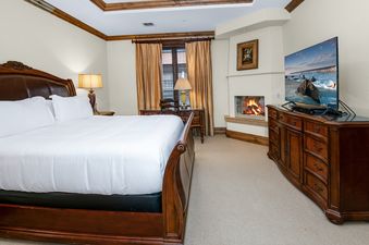 A luxurious bedroom in Arrabelle 460 features a king-sized sleigh bed, a fireplace with a lit fire, and a television.