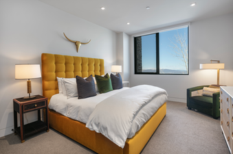 A bedroom with a plush yellow bed, white bedding, and a large window with a view of snow-capped mountains.
