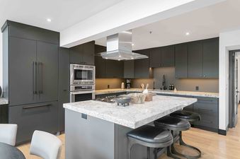Modern kitchen with dark gray cabinets, a large granite-topped island with bar stools, and stainless steel appliances at Queen Esther 2366.