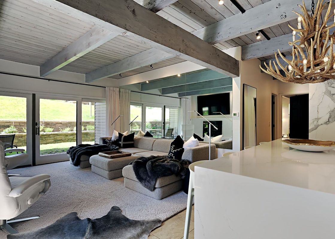 The living room area of Timberline Two Bedroom D2H, featuring a large sectional sofa, a fireplace, and floor to ceiling windows with views of the outdoors. The home is decorated with a modern farmhouse style with a fireplace, large windows, and a white se