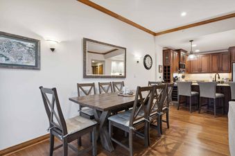 A dining room with a wooden table and chairs, a mirror on the wall, and a kitchen in the background.