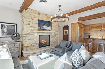 A cozy living room in Silver Strike Lodge 302 features a stone fireplace, a flat-screen TV, comfortable seating, and a view into the adjacent kitchen.