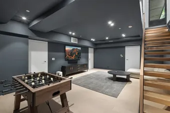 A modern games room in Maison Cornet featuring a foosball table, a wall-mounted TV, and wooden stairs.